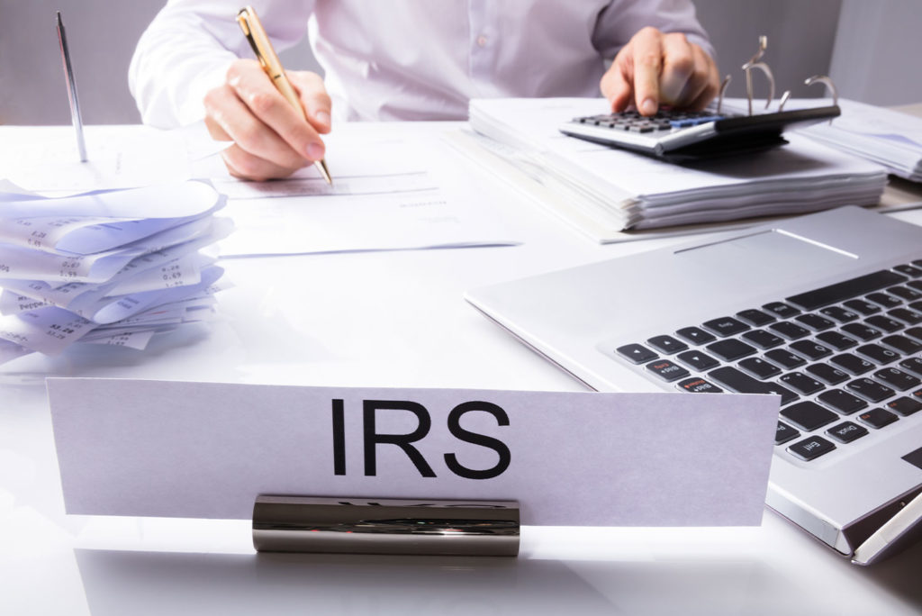 IRS agent auditing a business tax filing while at his desk with large IRS sign on it