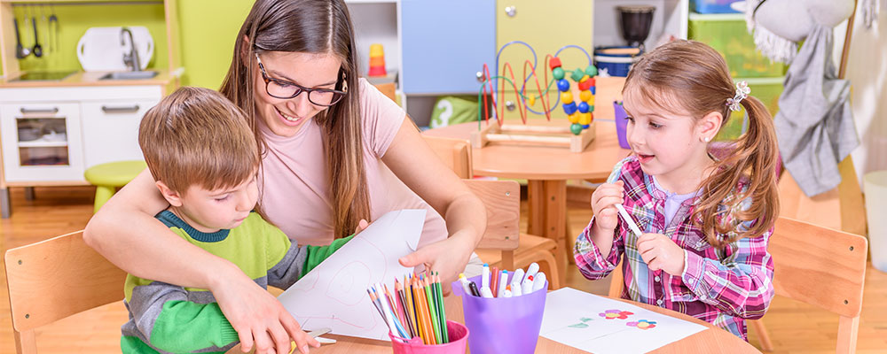 teacher making crafts with two young children in classroom