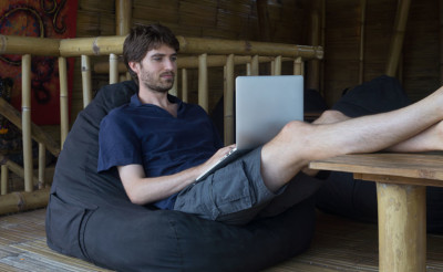 A male working on a laptop while sitting on a bean bag. 