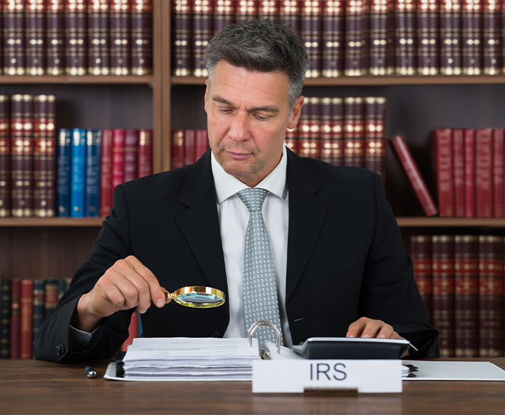 photo of businessman with a magnifying glass looking at IRS rules and regulations